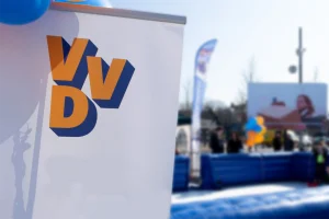 De oranje-blauwe letters van het VVD partijlogo op een banner, buiten bij een verkiezingsstunt